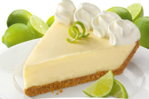 Key lime pie on a white plate with limes behind it.