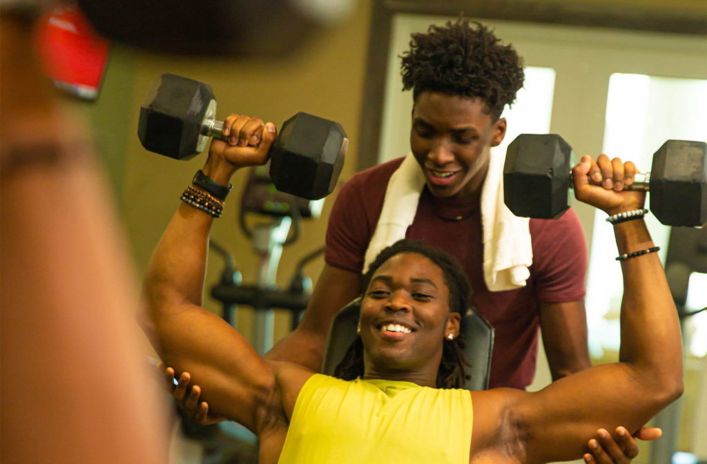 Young man lifting weights with a friend spotting in the Encore Resort fitness center.