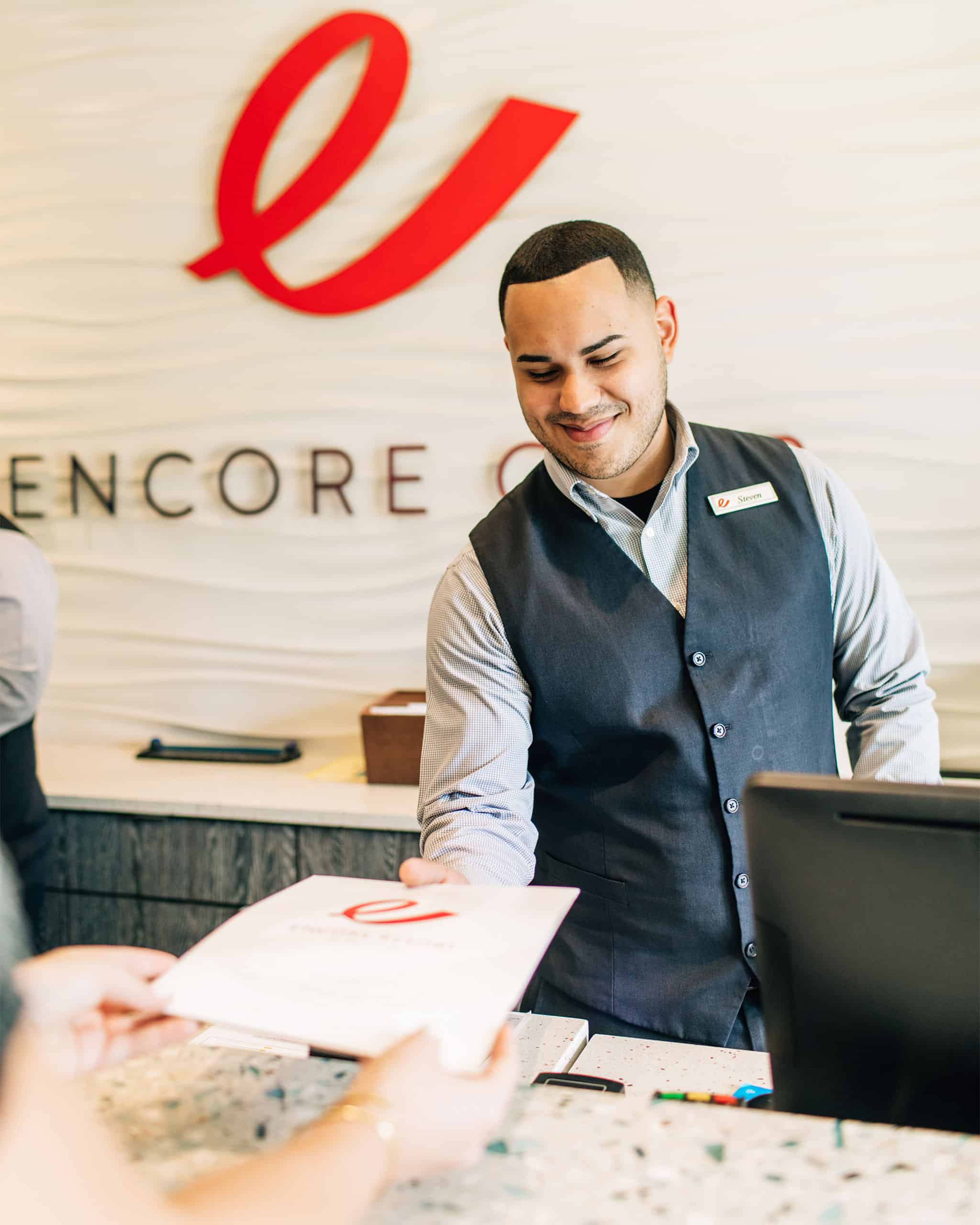 An Encore Resort concierge staff member smiles as he hands a guest information about their vacation home rental.