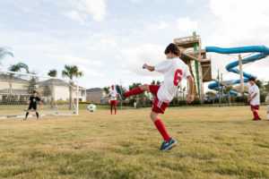 बच्चे फुटबॉल खेलते हैं Encore रिज़ॉर्ट खेल का मैदान, पृष्ठभूमि में एक्वा पार्क में पानी की स्लाइड के साथ।