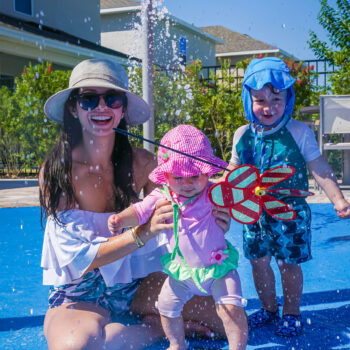 A mother and two toddlers smiling as they play at the Encore Resort East Side splash area.