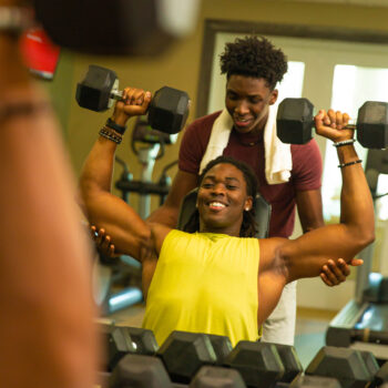 Young man lifts weights as a friend spots him inside the Encore Resort fitness room.