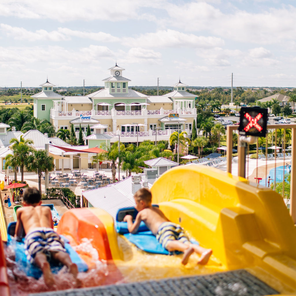 Двое детей готовятся к спуску с водной горки Wave Racer, Encore Resort Вдалеке клубный дом.