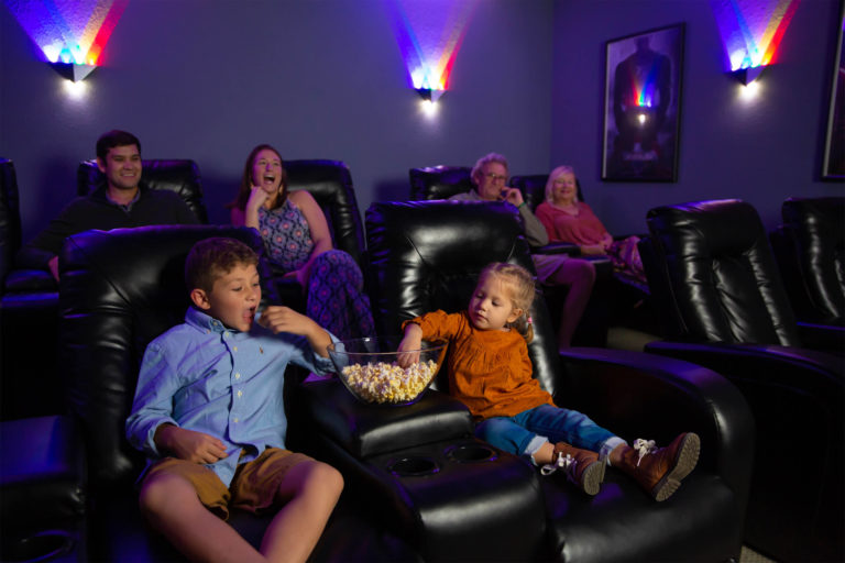 दो बच्चों वाला एक परिवार अंदर फिल्म देखते समय पॉपकॉर्न साझा करता है Encore रिज़ॉर्ट छुट्टी होम थियेटर।