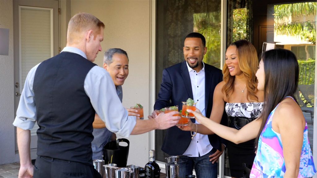 A group clinks glasses in a toast during an Encore Resort in-home bartender experience.