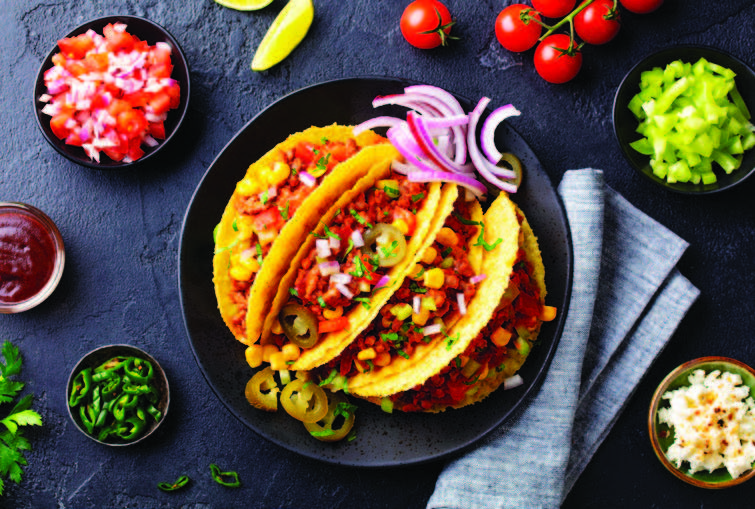 Hard and soft-shell tacos on a skillet with various toppings.