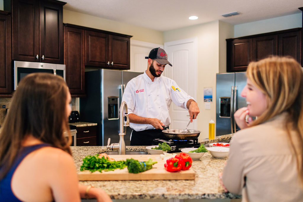Two women watch as a chef prepares a meal in their Encore Resort home.