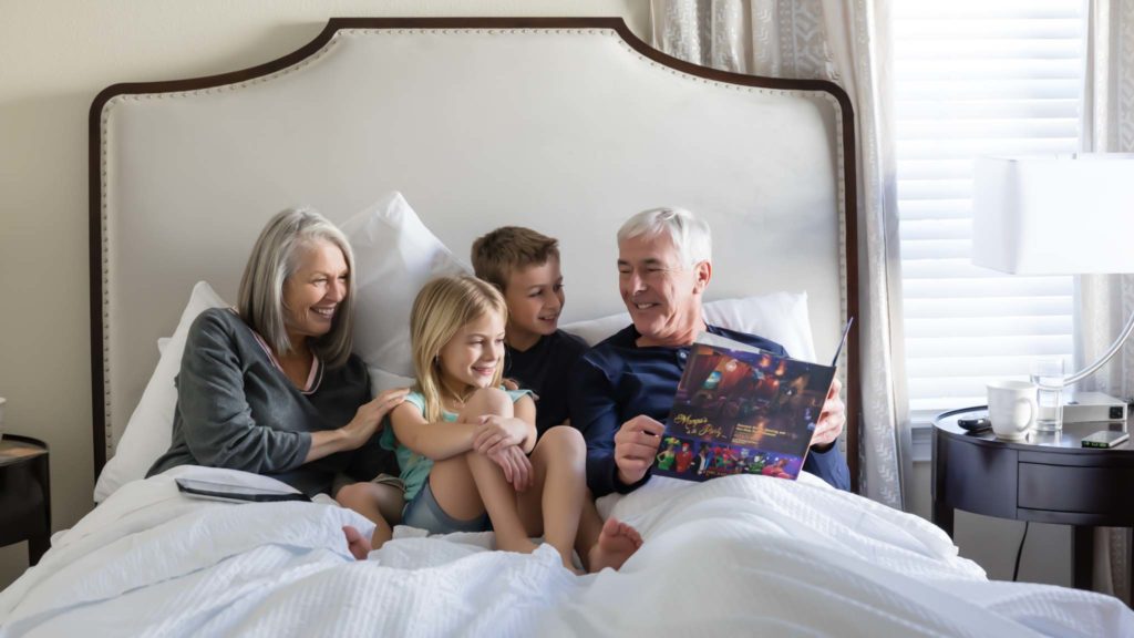 Großeltern lesen ihren kleinen Kindern in einem großen King-Resort-Bett vor.