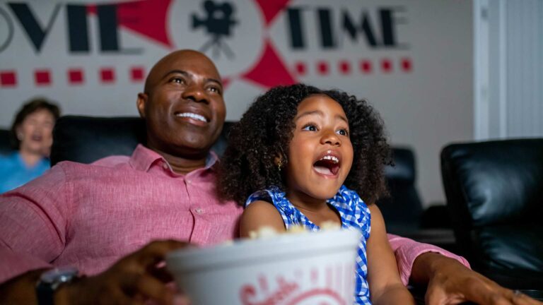 Father and daughter watching a movie while eating popcorn.