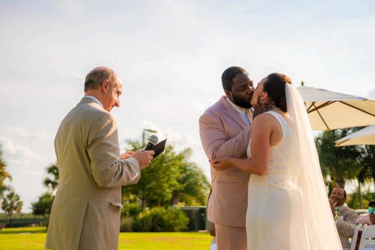 Les mariés s'embrassent pendant la cérémonie de mariage le Encore Pelouse pour événements de villégiature