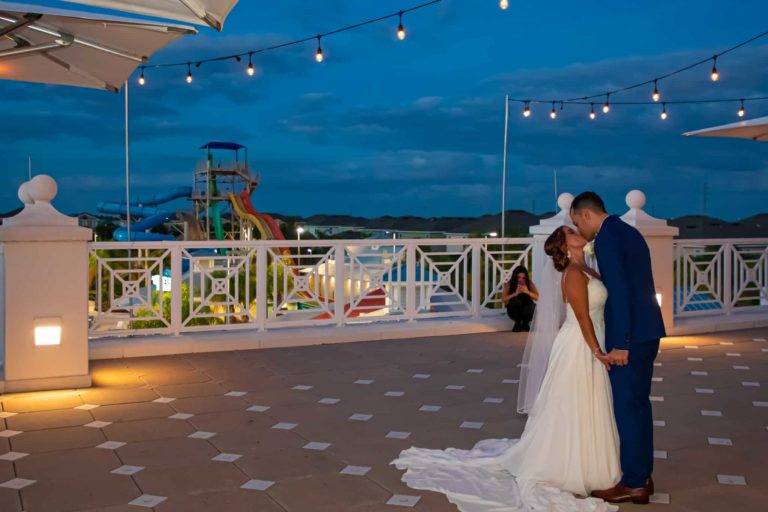 Les mariés s'embrassent sur le Encore Terrasse du Resort Clubhouse avec parc aquatique en arrière-plan