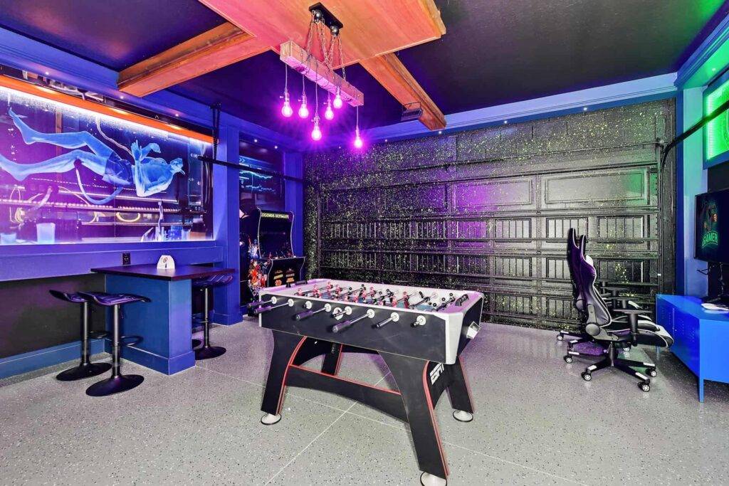 غرفة ألعاب ذات طابع مستقبلي مع ثريا ذات إضاءة سوداء وطاولة كرة قدم وخزانة أركيد ومحطة ألعاب فيديو