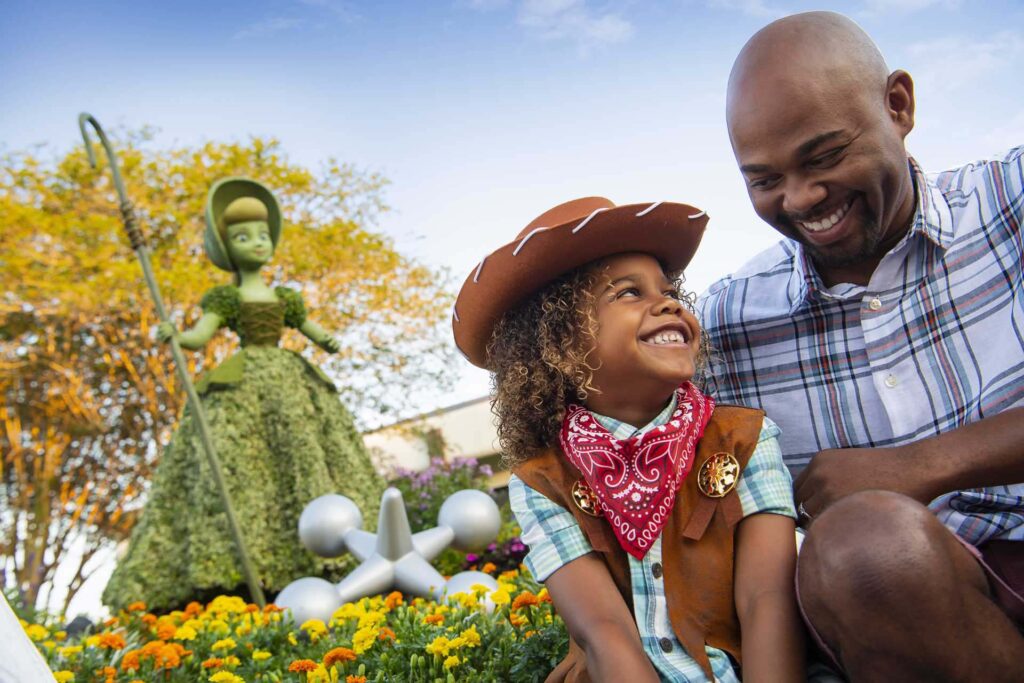 Father and daughter sitting by a Toy Story topiary at the EPCOT Flower and Garden Festival