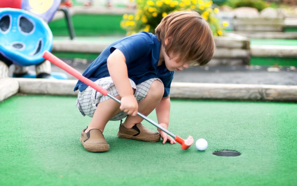 छोटा लड़का मिनी-गोल्फ़ खेल रहा है