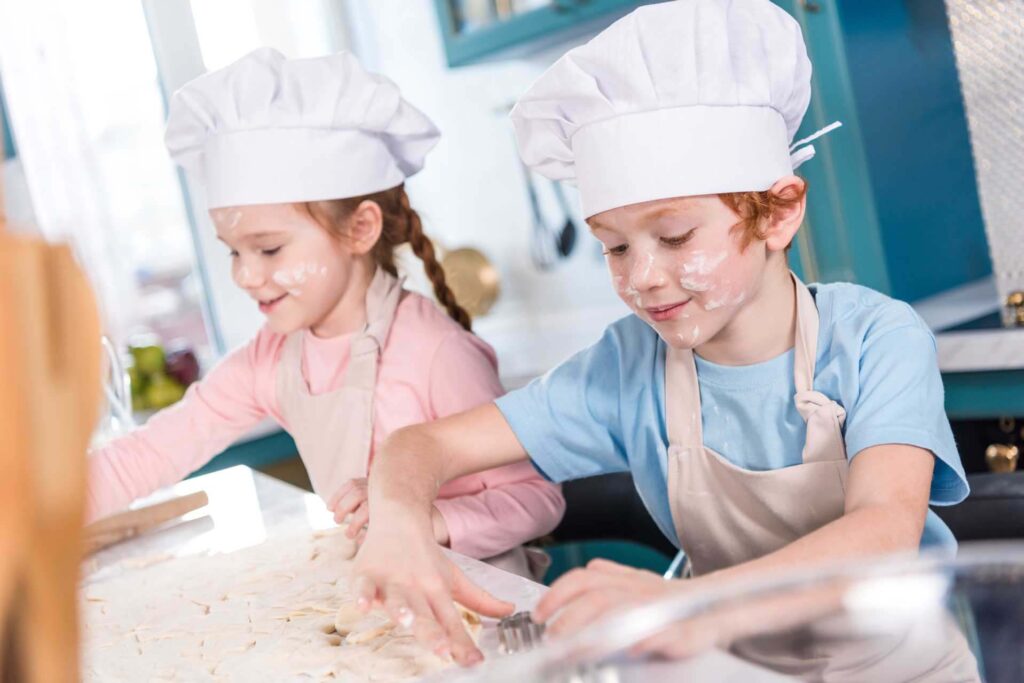 Crianças em chapéus de chefs e aventais fazendo biscoitos