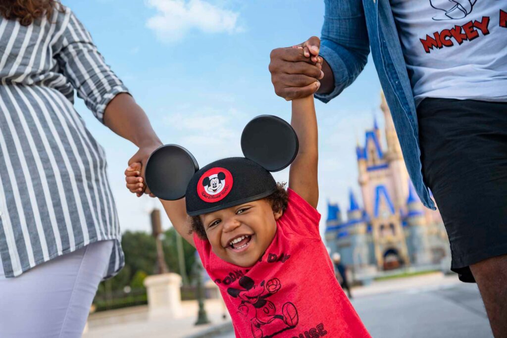 Happy, young child holding parents' hands while walking in front of Cinderella's Castle at the Magic Kingdom | Walt Disney World