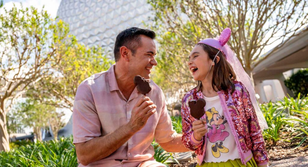 Father and daughter enjoying Mickey Mouse ice cream bars near Spaceship Earth at EPCOT | Walt Disney World
