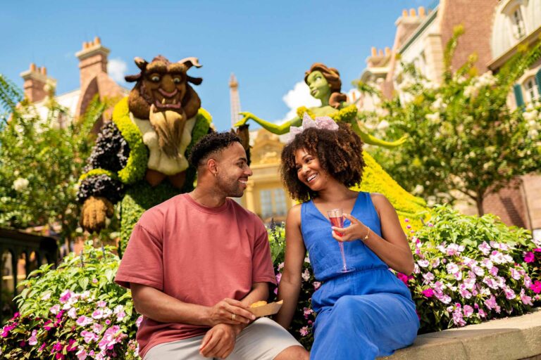 Happy couple with food and drinks in front of a Beauty & the Beast topiary at EPCOT's Flower & Garden Festival