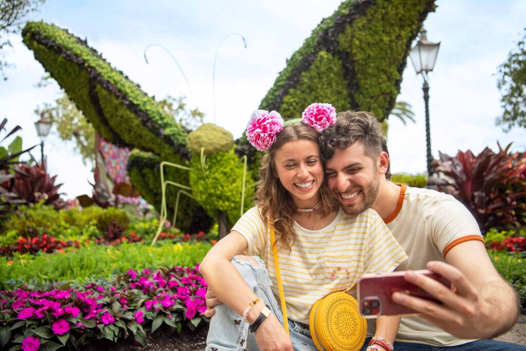 Pareja feliz tomándose una selfie frente a un topiario de mariposas en el Festival de Flores y Jardines de EPCOT