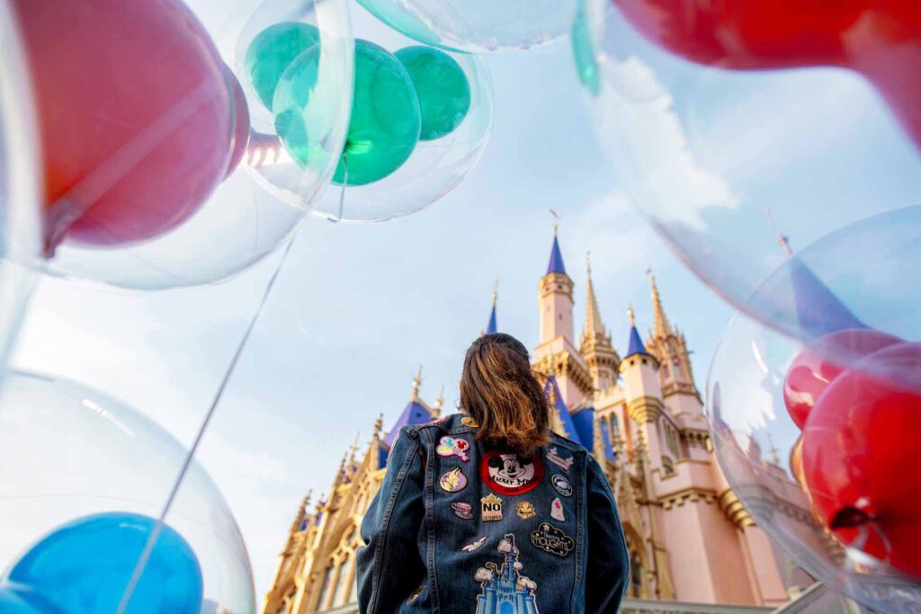 लड़की मैजिक किंगडम में गुब्बारों से घिरी सिंड्रेला के महल को देख रही है